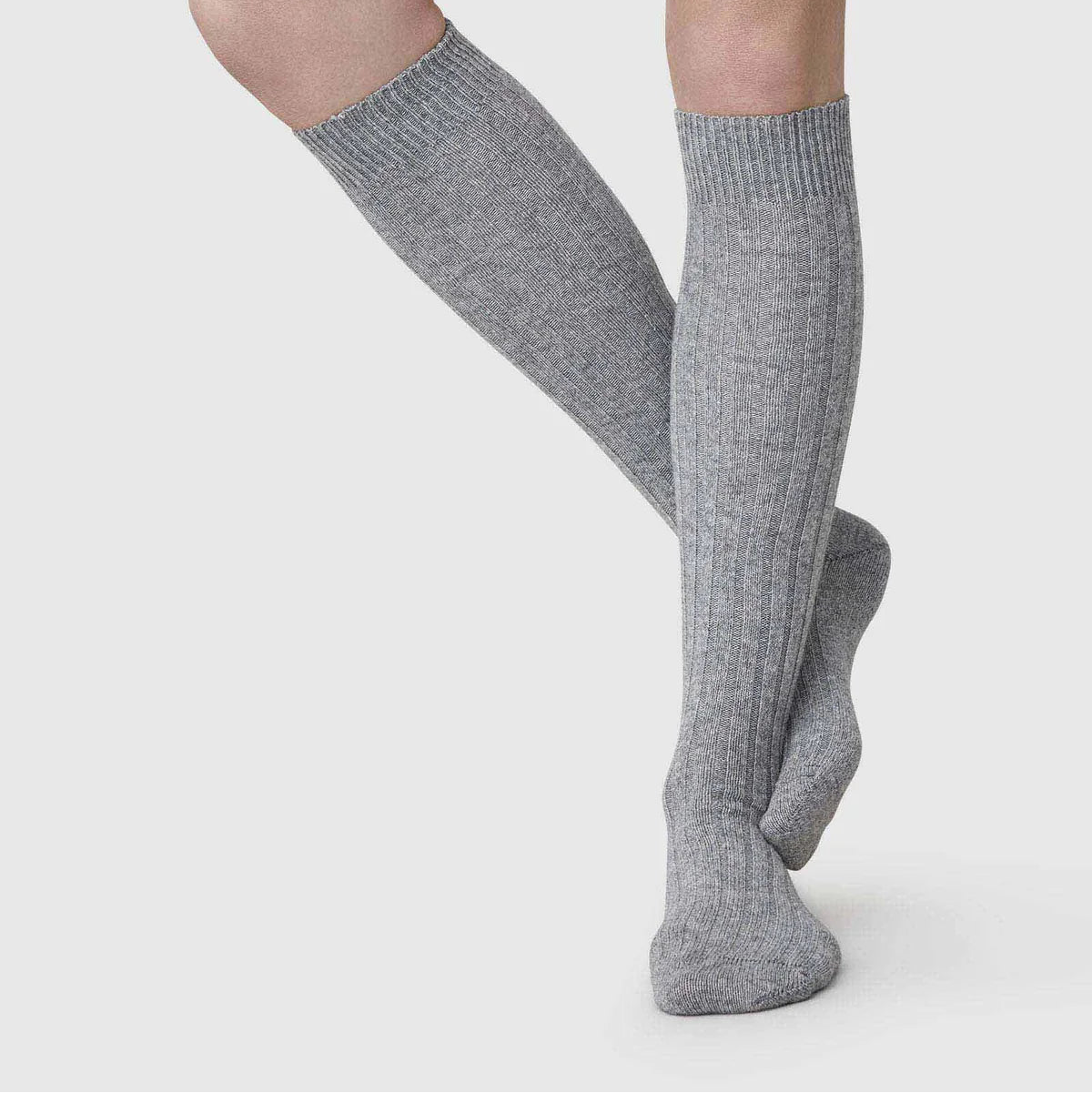 Gray knee-high socks worn by a person on a light gray background