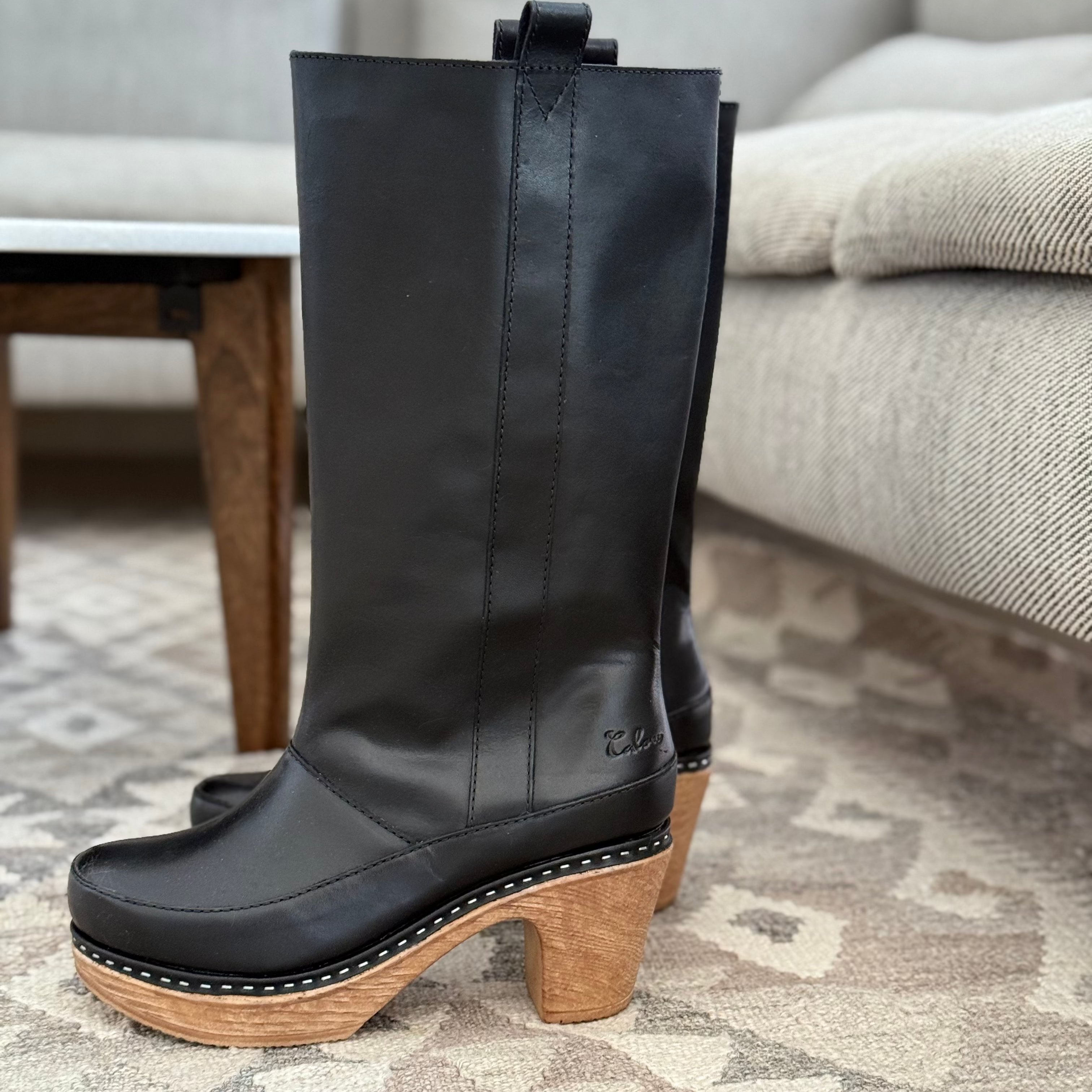 Black leather boot with wooden sole on a patterned rug
