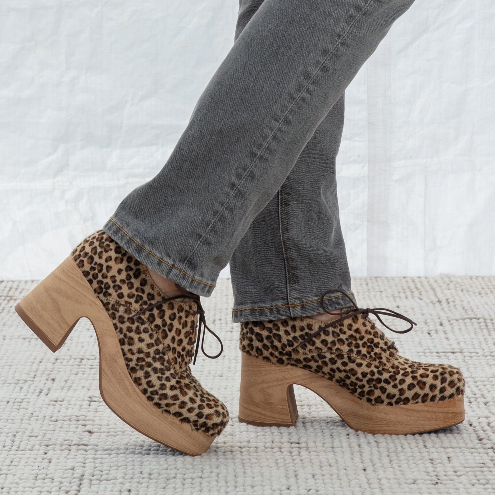 Leopard print clog shoes worn with gray jeans on a textured surface.