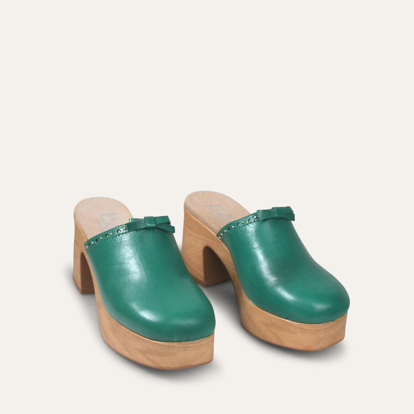 Green clogs with wooden sole on a light beige background