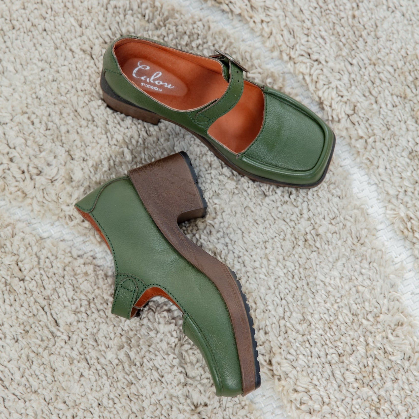Green clogs with brown soles on a beige carpet