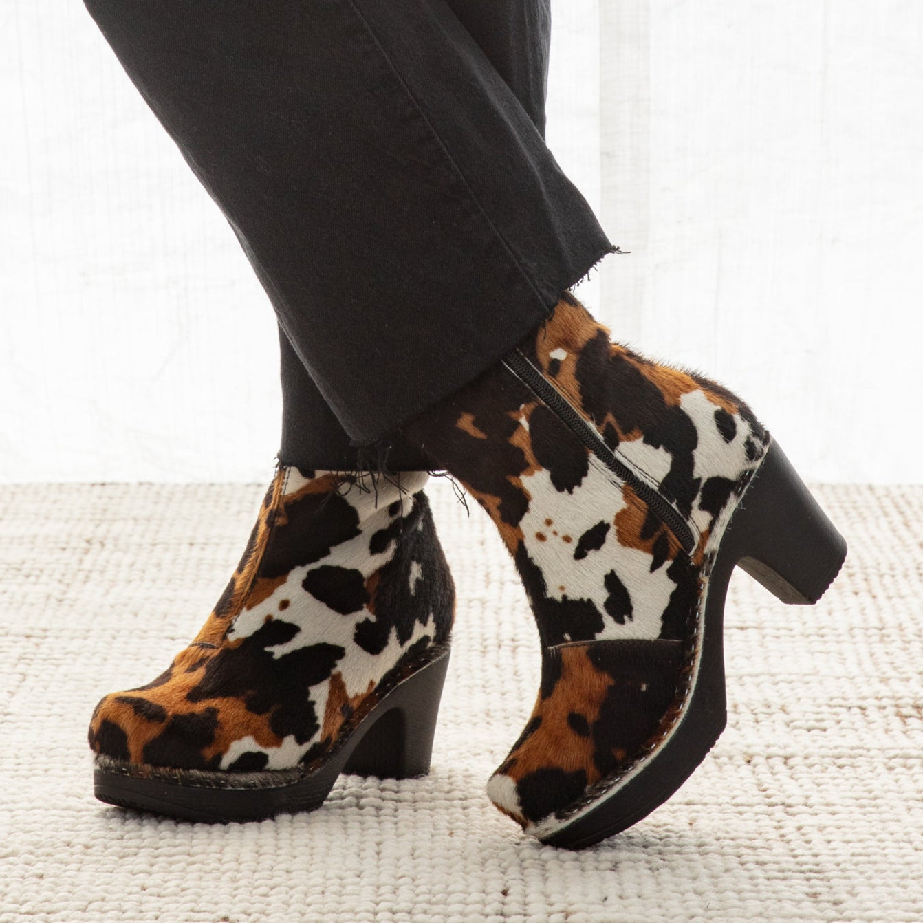 Cow print boots worn with black pants on a light background