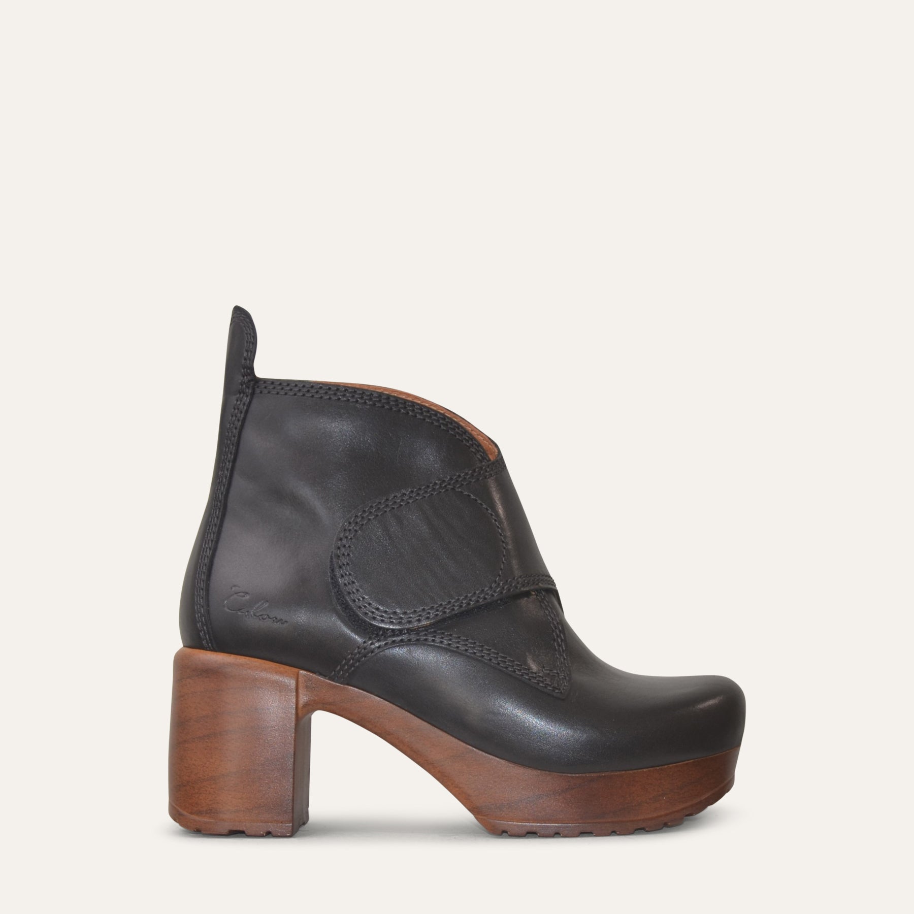 Black leather ankle boot with wood-like heel on a light gray background