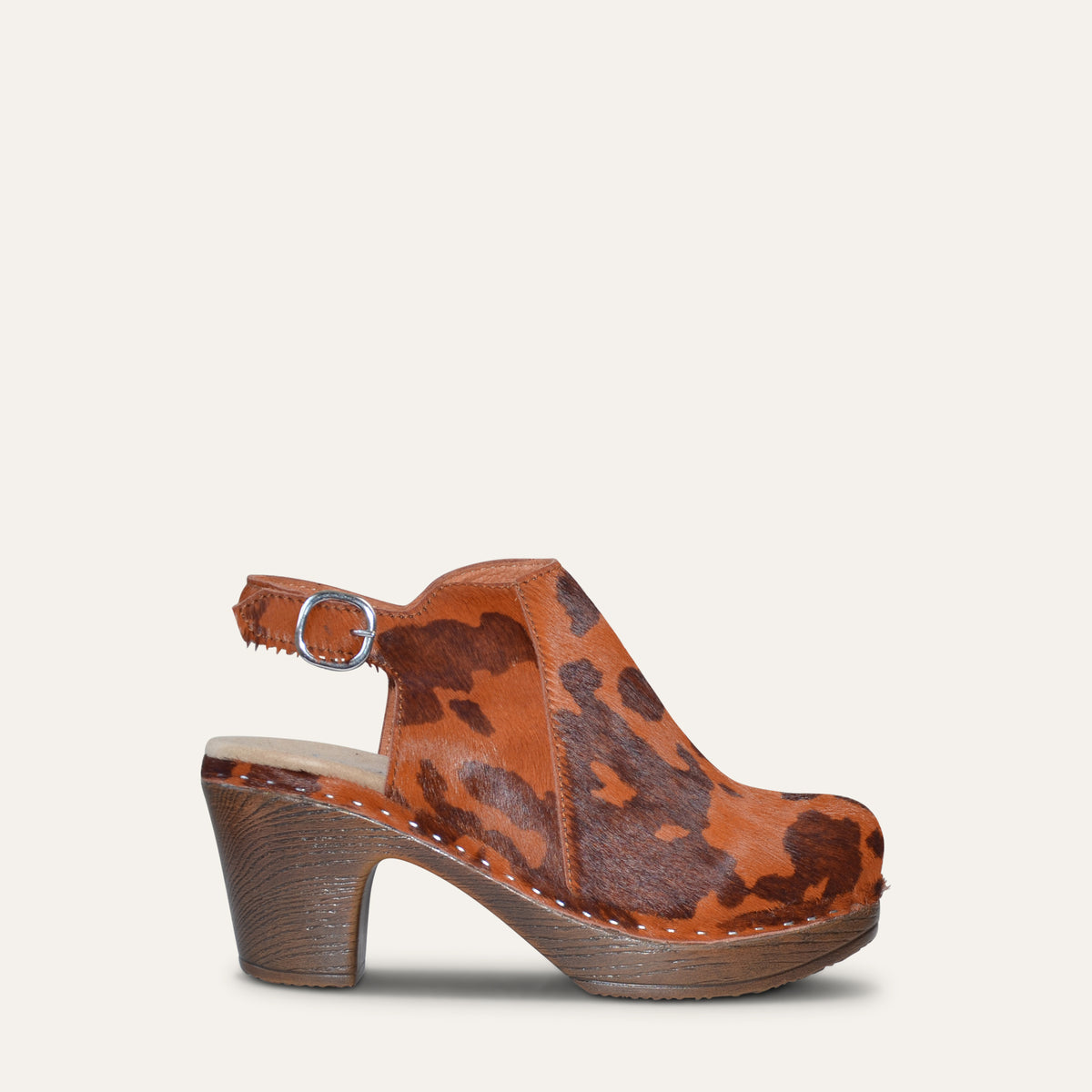 A single women's clog sandal with a brown and orange cowhide pattern upper, a chunky brown soft, flexible block heel, and an adjustable ankle strap with a silver buckle, shown against a light beige background.